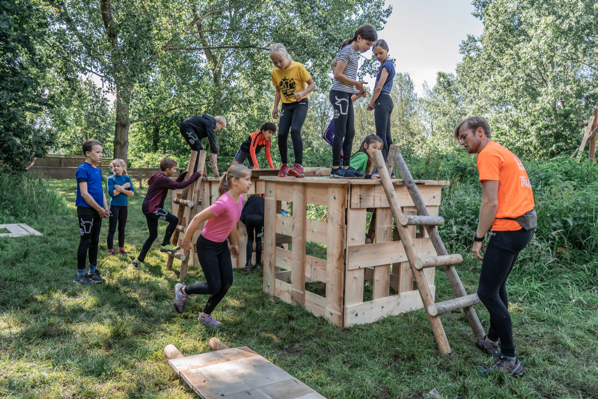 Kinderen bouwen samen aan hutten in de speeltuin.