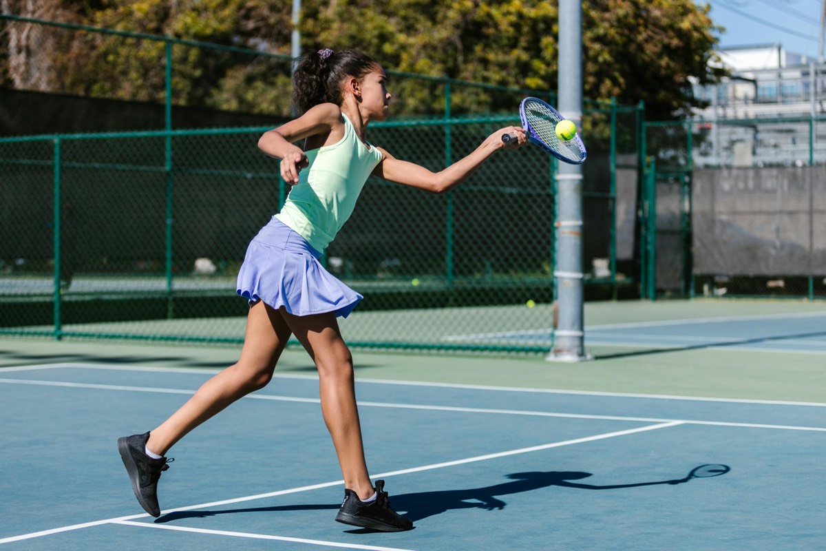 Een meisje slaat een tennisbal op een vernieuwde tennisbaan.